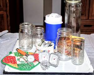 lot 8334 image: Assorted Kitchen Wares Lot, Metal Enamel Wares Tray, Jars and Lids, Fridge and Meat Thermometer, Brand New Coleman Travel Jug, Glass Cannister, Picture Magnet, Vtg Pot Holders and More