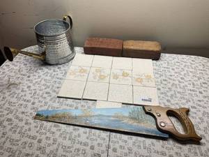 lot 8085 image: Lot of Assorted Decor Items  Includes Metal Watering Can, Painted Saw, 13 Tiles, and 2 Bricks