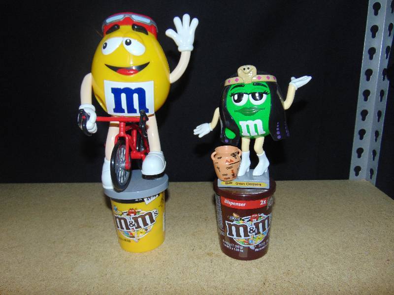 lot 4044 image: (2) ct. lot M&Ms Candy Dispensers (1) Cleopatra Green, approx 9 tall  (1) Yellow on a bicycle, approx 11 tall