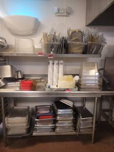 lot 18659 image: Contents of Dish Table and Shelf - Assortment of Stainless-Steel Steam Table Pans, Large Food Storage Bins, Condiment Bottles, and More