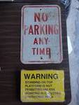 Metal No Parking Any Time sign and a stack of wrapped/new metal Warning Signs