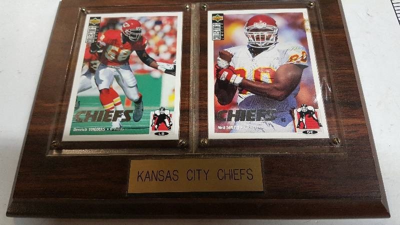 lot 5839 image: Kansas City Chiefs Derrick Thomas and Neil Smith Player Trading Cards mounted and protected on a nice wooden plaque .