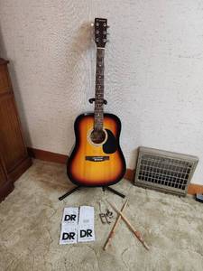 lot 24 image: Dinosaur Acoustic Guitar (model DAG-3BS), Guitar Stand, Extra String, Drumsticks, and More