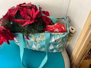 lot 2676 image: Christmas thirty one bag filled with Christmas items including a light up poinsettia, ornaments, coffee mugs, holiday banners and a candle with a festive nutcracker holder