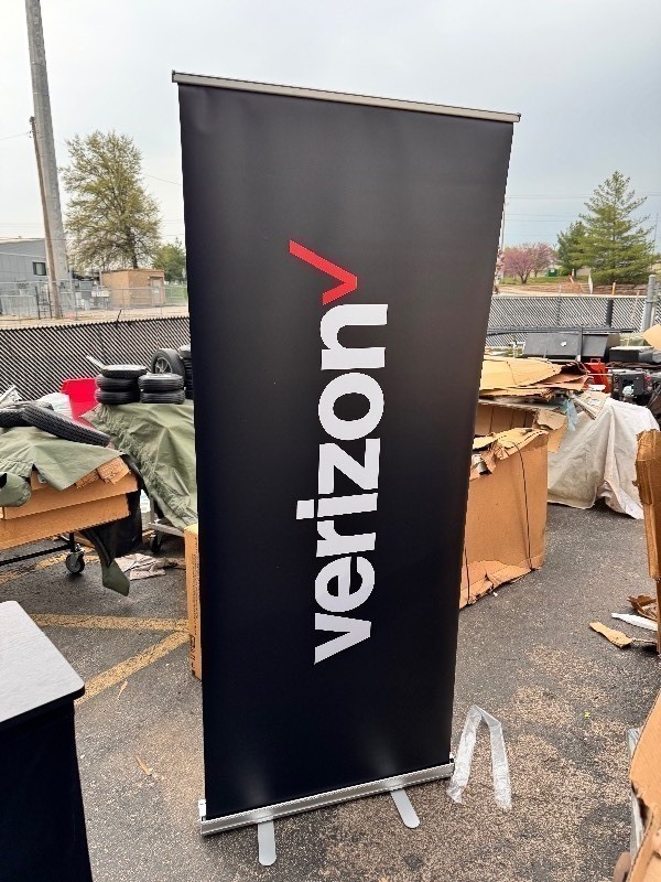 lot 184 image: New 8x34 Retractable Stand Alone Backdrop Banner w Travel Bag , Black. Comes as pictured as is can put your own fabric on it or remove the Verizon logo.