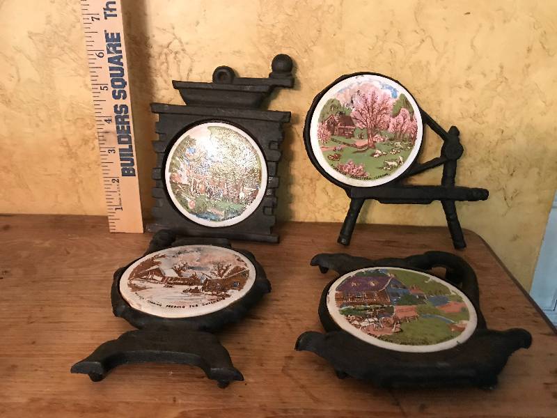 lot 50 image: Ceramic and Cast Iron Trivets--with country scenes and shapes (coffee grinder, spinning wheel, etc)