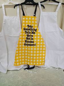 lot 84 image: Wizard of Oz Yellow Gingham Apron with Quote and two white aprons