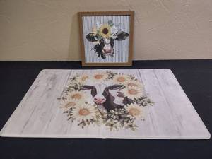 lot 344 image: Farmhouse Cow padded kitchen floor mat (has a crease in center) and Sunflower Cow Wall Art with Ridged Tin Back