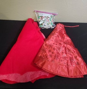 lot 373 image: Two Christmas tree skirts, one shiny red with snowflake pattern, one red felt, and a bag of candy cane lights.
