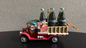lot 254 image: 1992 Coca-Cola Christmas ornament featuring a gnome driving a red delivery truck with a crate of miniature Coca-Cola bottles.