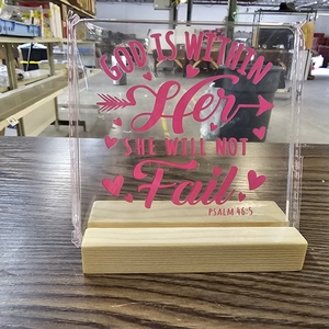 lot 2844 image: Christian-themed decorative acrylic sign featuring the Bible verse Psalm 465, God is within her, she will not fail. This tabletop ornament consists of a transparent acrylic plaque with pink-toned lettering and heart accents, set into a light-colored wo