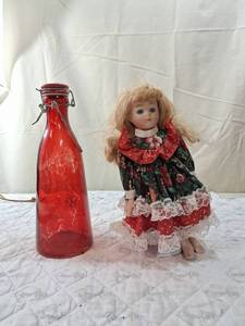 lot 84 image: Porcelain Doll in Floral Dress with Red Glass Bottle