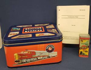 lot 71 image: Large Lidded Lionel Train Advertising TinContainer - 14in W x 10in D x 8in T, Vintage Fossil Watch Box Tin with Train Design, and 2007 Department of The Army Fundamentals of Flight Manual