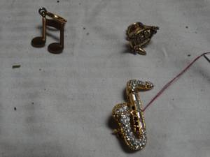 lot 24978 image: Rhinestone encrusted gold tone saxophone brooch, Music pendant and clock house earring.