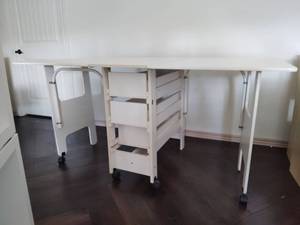 lot 1001 image: White Folding Drop Leaf Sewing Craft Table with Storage Cart Top will need reattached 35x72x40 in at its largest Located in Basement