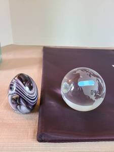 lot 1047 image: Moderna art glass crystal frosted paperweight globe with a blue bandage over the United States and a grey egg-shaped paperweight