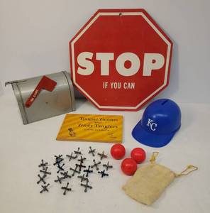 lot 172 image: Vintage 1970s True Scale  Pressed Metal Mail Box Bank, 1973 KC Royals Baseball Cap Bank, 1975 Tongue Twisters and Tricky Tanglers Book, Vintage Ball & Jacks Game Pieces, and Humorous Stop Sign 10in x 10in