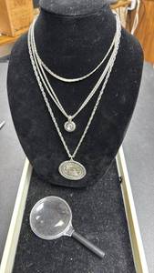 lot 104 image: Three Silver Toned Necklaces, one with Liberty Bell Pendant and one with Small Stone Charm.  And a Magnifying Glass