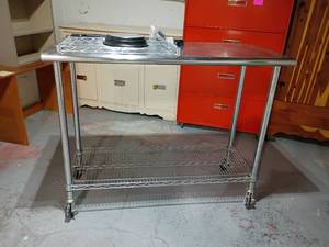 lot 958 image: Stainless Steel Prep Table with Locking Wheels an Extra Wire Shelf and Clock.   Shelf doesnt go with table    Table 39 x 50 x 24.   Located in basement