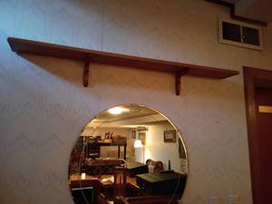 lot 998 image: Wooden Shelf and Round Decorative Mirror.   Shelf 48in long.  Mirror is 27in diameter.  Both will need removed from wall.   Located in basement