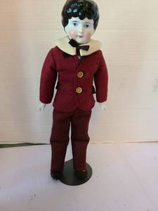 lot 1047 image: Porcelain Head Doll with Black Hair Red Outfit Cream Collar, 12in tall on stand