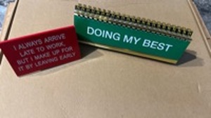 lot 628 image: Flip-Through Funny Desk Sayings (50 Different ones) with Gold Spiral Binding and Red Plastic I ALWAYS ARRIVE LATE TO WORK, BUT I MAKE UP FOR IT BY LEAVING EARLY Sign. - Retail $18