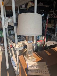 lot 155 image: Metallic obelisk table lamp featuring a tapered silver-tone base and a neutral beige drum shade.