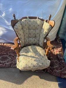 lot 97 image: Wooden wingback gliderrocking chair with light-colored, floral-patterned upholstered cushions