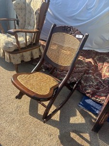 lot 98 image: Vintage wooden folding rocking chair featuring a woven cane seat and back with a carved floral headrest