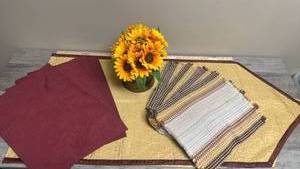 lot 660 image: Dining table decor lot. Includes two sets of placemats, a table runner and a hammered brass pot with sunflowers