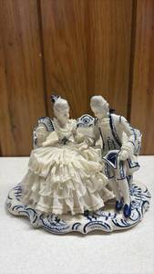 lot 163 image: Vintage blue and white porcelain figurine featuring a courting Victorian or 18th-century royal couple (often styled as Marie Antoinette and King Louis or a colonial courting scene) seated on a loveseat with delicate applied lace-style detailing.