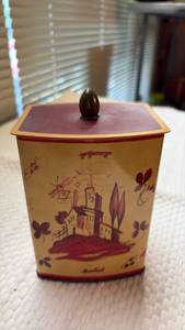 lot 1012 image: Vintage West Germany tin storage container featuring a charming yellow body with a red decoration of a rustic European cottage and topped with a distinct onion-shaped knob lid.