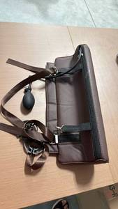 lot 146 image: Brown padded leather-like shoulderbody bag with adjustable straps, zipper closure, metal buckles, and an attached black rubber air bulb and tubing. Overall appears to be in good condition with minor creasing from storage. - Retail $0