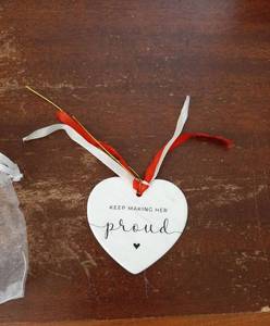 lot 29043 image: 2 Pack of Keep Making Her Proud Heart Ornament with Red and White Ribbons White heart-shaped ornament with printed text reading KEEP MAKING HER proud and a small heart symbol. Attached with red and white ribbon loops for hanging. - Retail $9