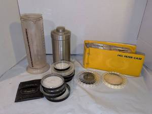 lot 3126 image: Nikor developing tank, plastic beakers, empty round filter cases, some filters, and a flat case with additional filters