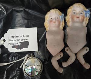 lot 927 image: Mother of Pearl with Mt. scene Pendant and Pair of Bisque Doll Heads with Blonde Hair and Blue Ribbons and misc arms.