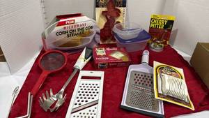 lot 1091 image: Microwave corn steamer, cherry pitter, cookie cutter and slicer all new in pkg, cheese shredder, strainer and spoons