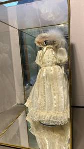 lot 1326 image: Porcelain Doll 18 inches tall, with Cream Lace Dress and Hair Bonnet in glass and mirrored case.