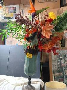 lot 34011 image: Autumn-themed faux floral arrangement featuring vibrant orange and yellow blooms set inside a tall teal pedestal vase