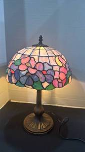 lot 1089 image: Faux Tiffany-style table lamp with a floral stained glass shade on a fluted bronze-finished metal base 18 inches tall