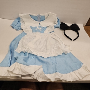 lot 2093 image: IWALUE Girls Alice in Wonderland Princess Costume, styled as a classic light blue dress with an attached white ruffled apron pinafore, large white Peter Pan collar, cross-ribbon chest detail, and an accompanying black bow headband. 3-4 Years