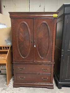 lot 35180 image: Wood armoire cabinet with two upper doors, oval panel accents, and two lower drawers at the base.