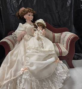 lot 1178 image: Porcelain Dolls 2-Piece Set Mother and Child Cream Lace Dresses displayed on burgundy upholstered settee. Very nice for the Mother in your life. - Retail $0