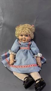 lot 525 image: Legacy Doll Inc Doll with Blonde Curly Hair, Blue Eyes, Blue Dress with Red Heart Trim Patent Shoes(approximately 11 inches seated)