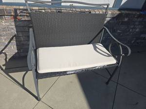 lot 4003 image: Outdoor wicker style bench, 39x 41x23 with white cushion, original seat has been damaged by sun, mended with duct tape.