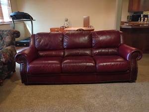 lot 922 image: Burgundy Colored Leather Couch with Brass Brads.  35in tall x 85in long.  Seats 22 x 22.   Located in basement