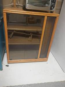 lot 981 image: Oak Stereo Cabinet on Wheels.   Glass Front, Holds CDs on side and Shelves on side too. 37 x 32 x 17.  Located in basement
