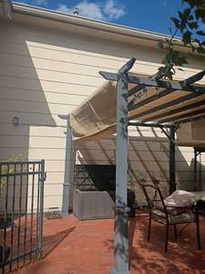 lot 998 image: Outdoor Pergola Structure with Tan Canopy and Black Frame.  7ft. 9in x 10ft x 10ft.  Bring tools and help to remove this item