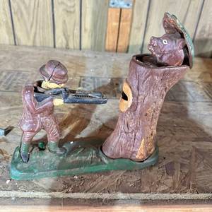 lot 10 image: Painted Figural Bank, Hunter Aiming Rifle at Animal in Tree Stump