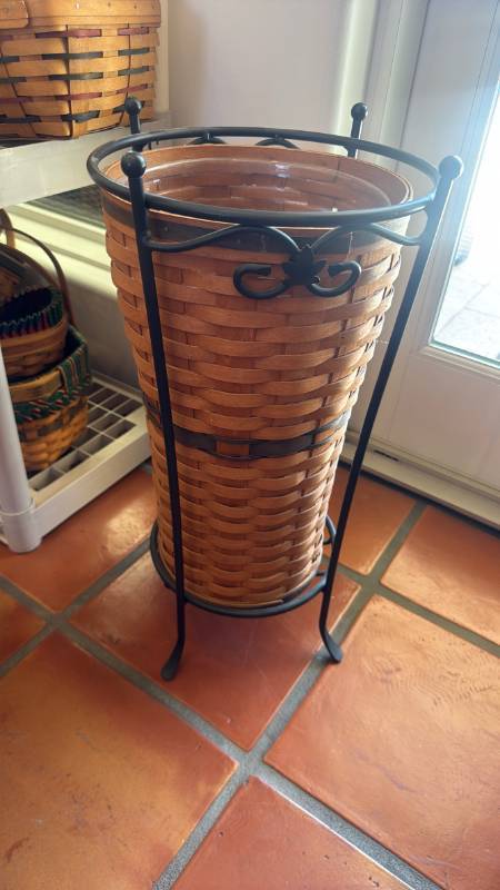 lot 1083 image: Longaberger Umbrella Basket paired with a black wrought iron stand 22 inches tall